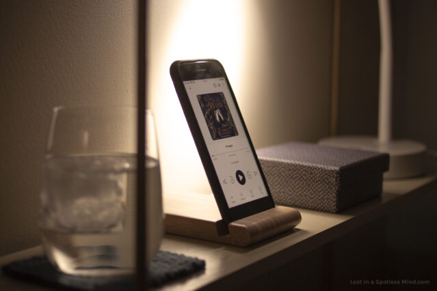 A moody photo of a phone in a bamboo holder, playing an audio book.