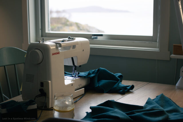 A sewing machine on a desk by a window, with teal fabric ready to sew.